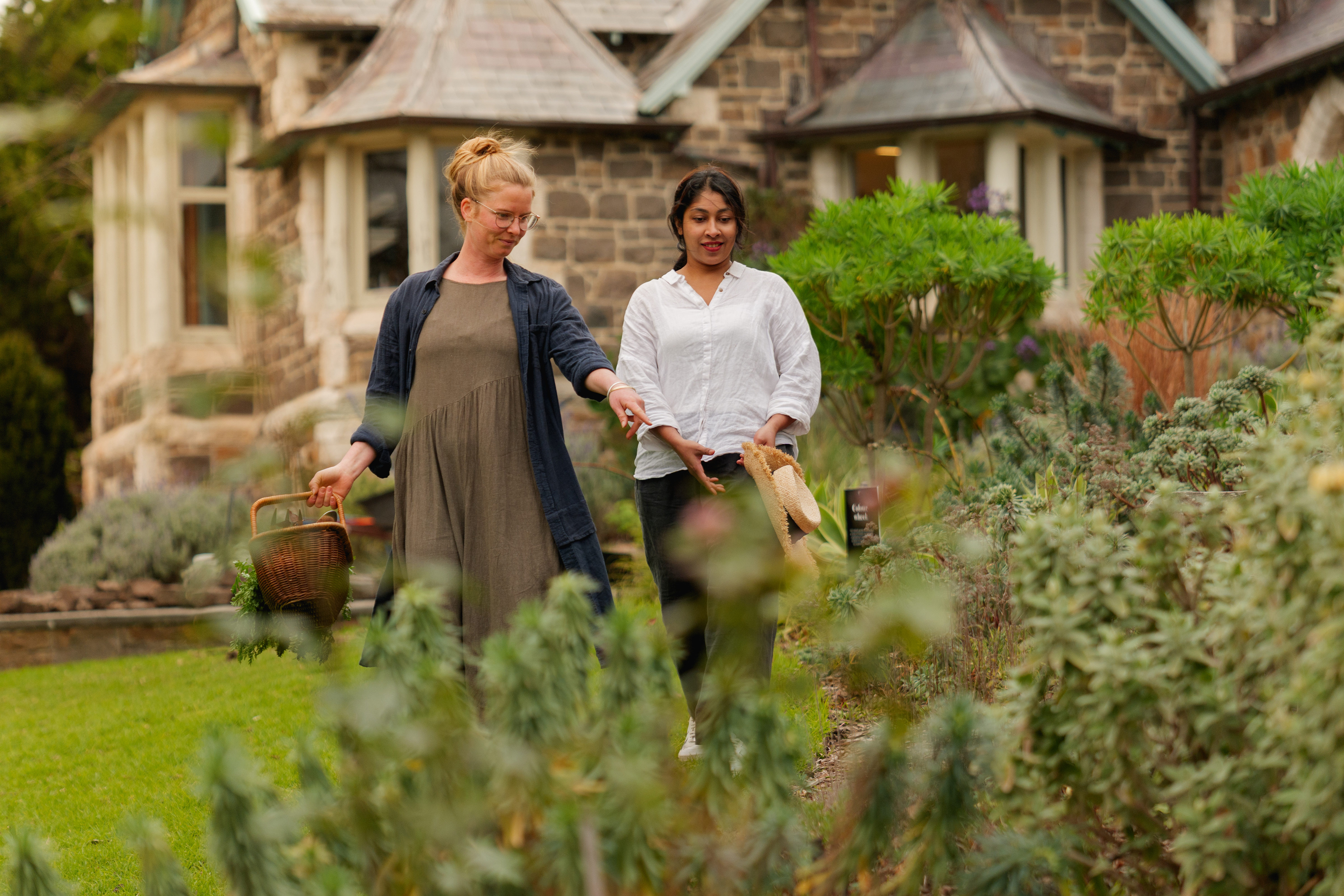 Two women point at a plant in a garden