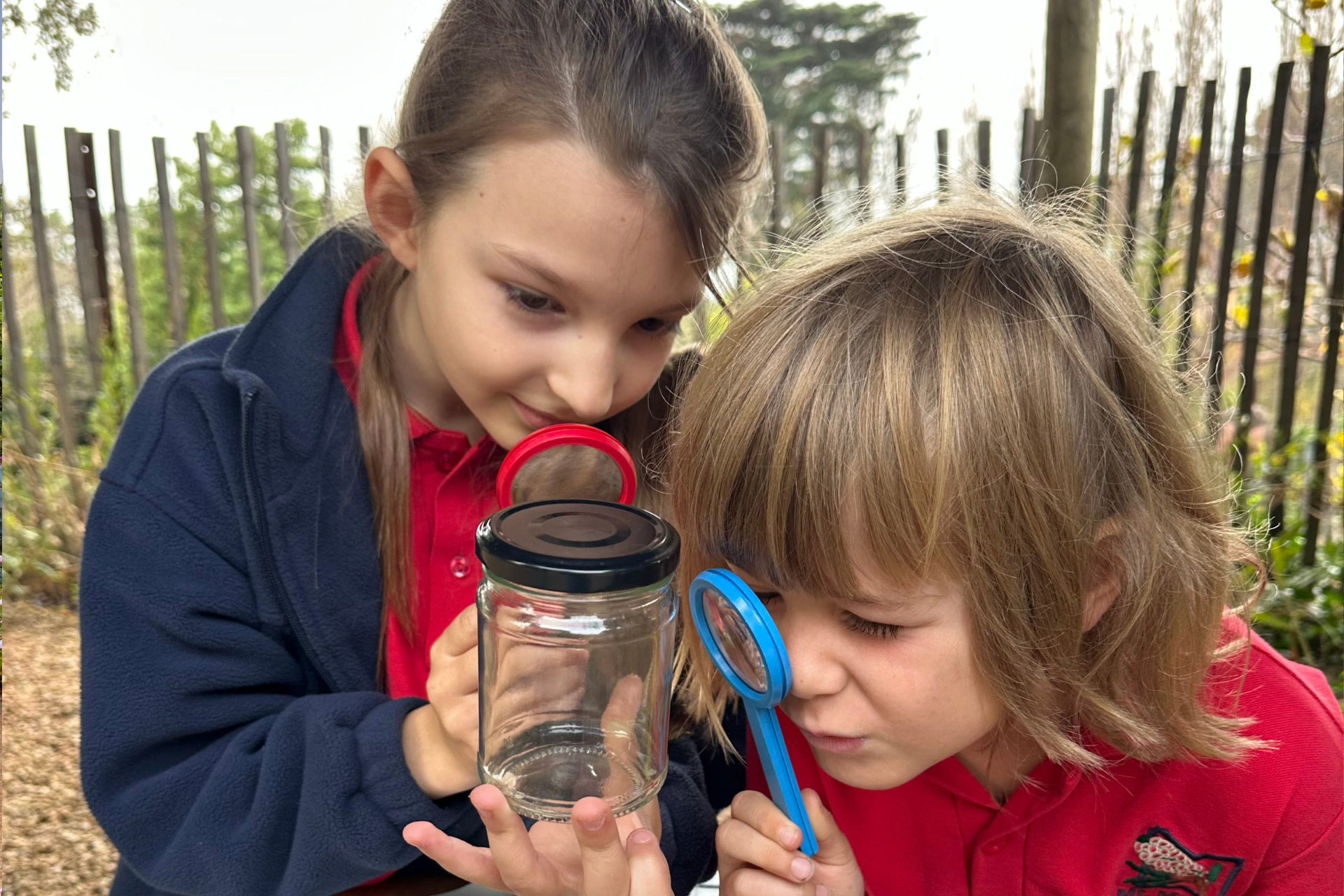 Two kids use magnifying glasses to examine a jar