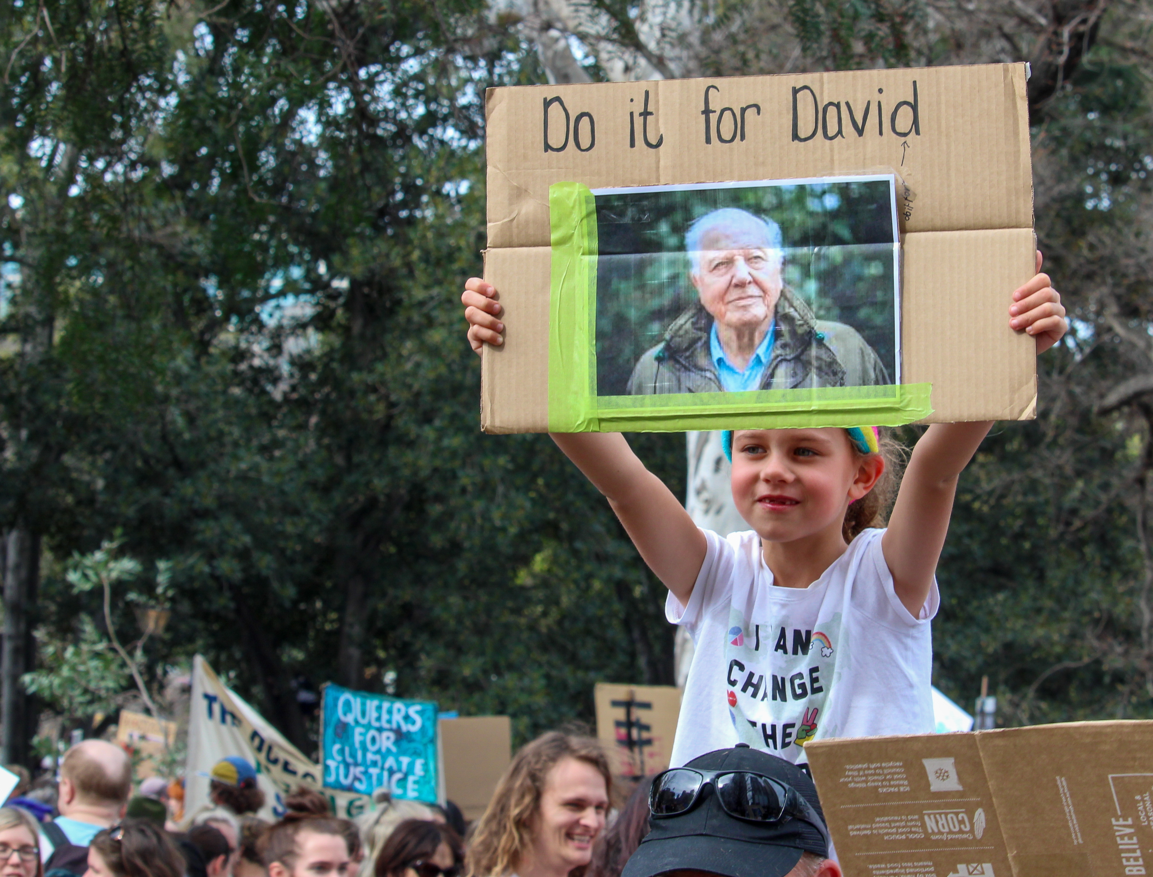 A young girl at a protest holds aloft a sign which reads 'Do it for David'