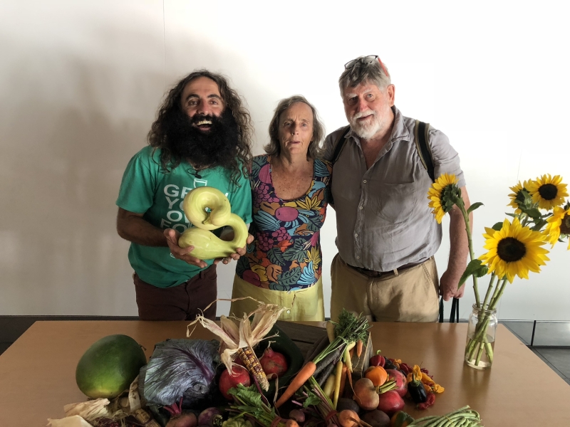 Three people smile for the camera behind a table covered in fresh produce